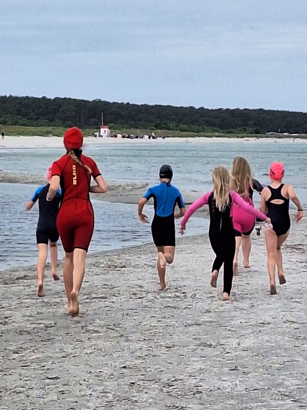 Kinder rennen in Neoprenanzügen über den Strand